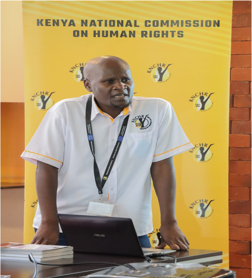 Commissioner Dr. Dennis Wamalwa addressing an audience beneath the Kenya National Commission on Human Rights banner